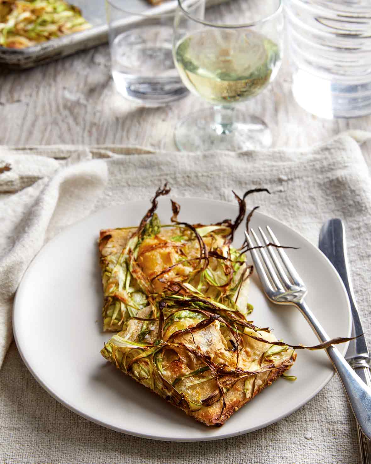 Plate with shaved asparagus pizza, fork and knife, on a kitchen towel