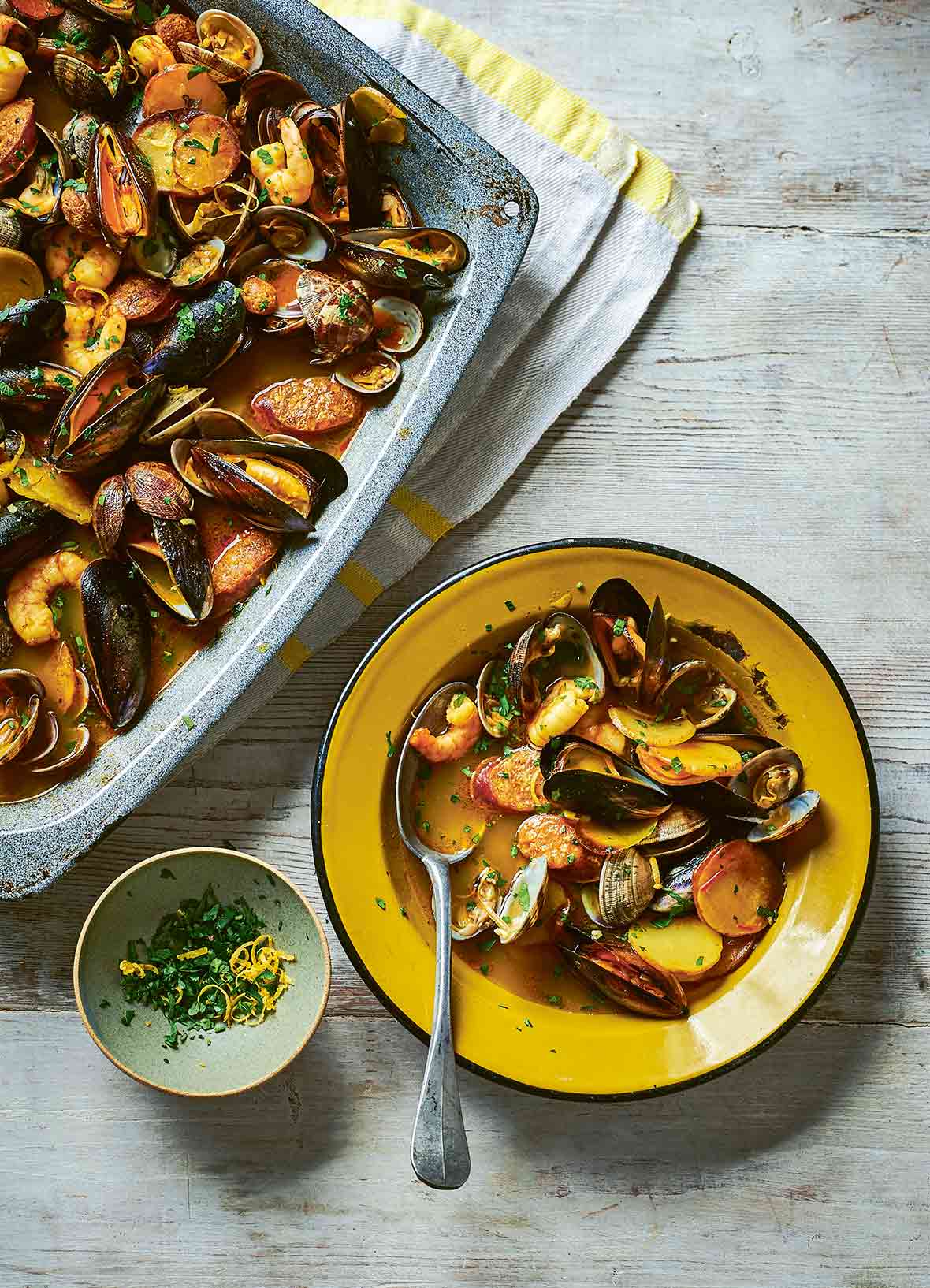 Sheet pan and a yellow bowl filled with seafood and chorizo stew of mussels, shrimp, clams, chorizo, and potatoes