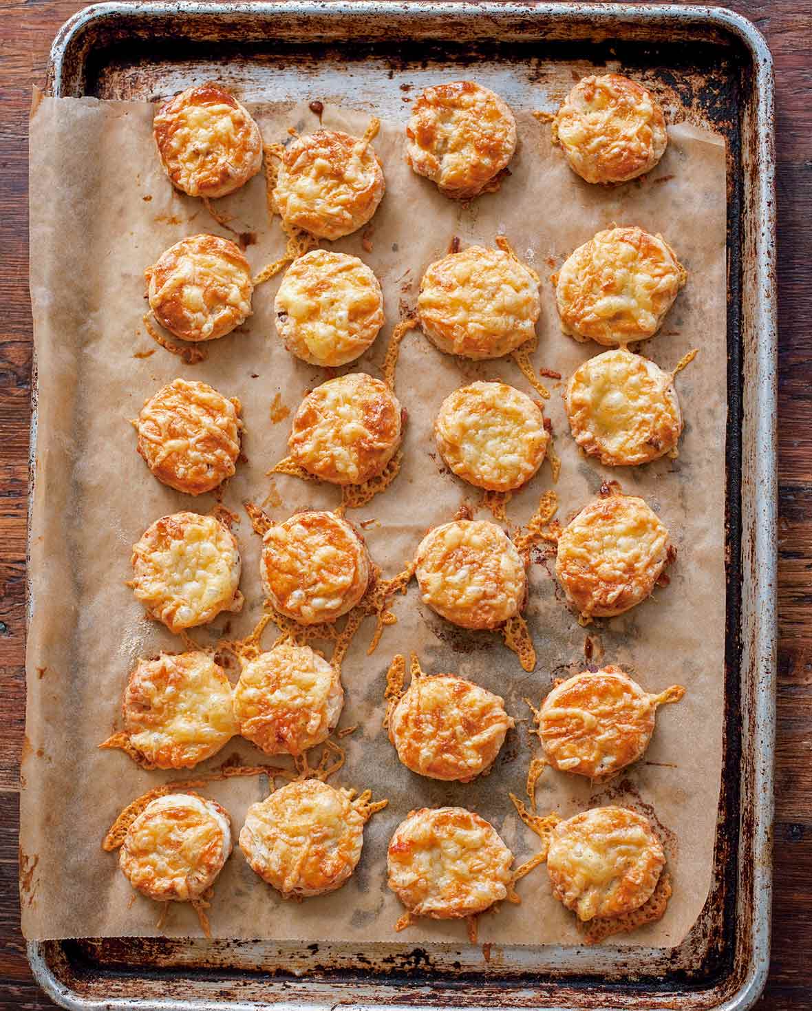 Bite-size bacon and cheese scones with smoked bacon and melted Asiago on top on a parchment-lined baking sheet