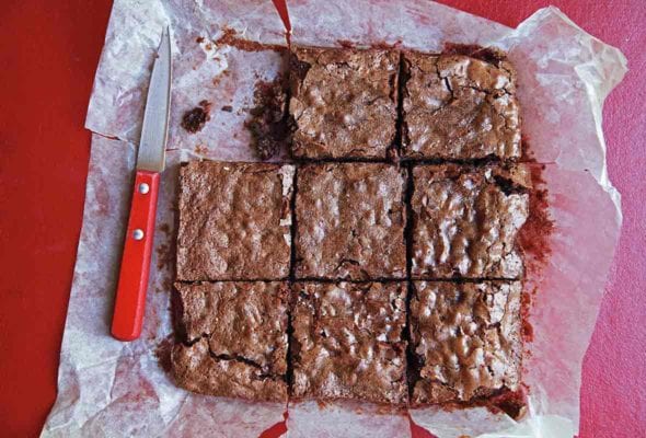 A slab of Katharine Hepburn brownies cut into 9 pieces, on parchment paper, with a knife nearby