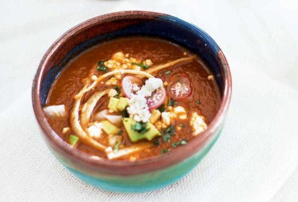 A pottery bowl filled with tortilla soup, garnished with radish, cotija cheese, tortilla strips, and avocado.