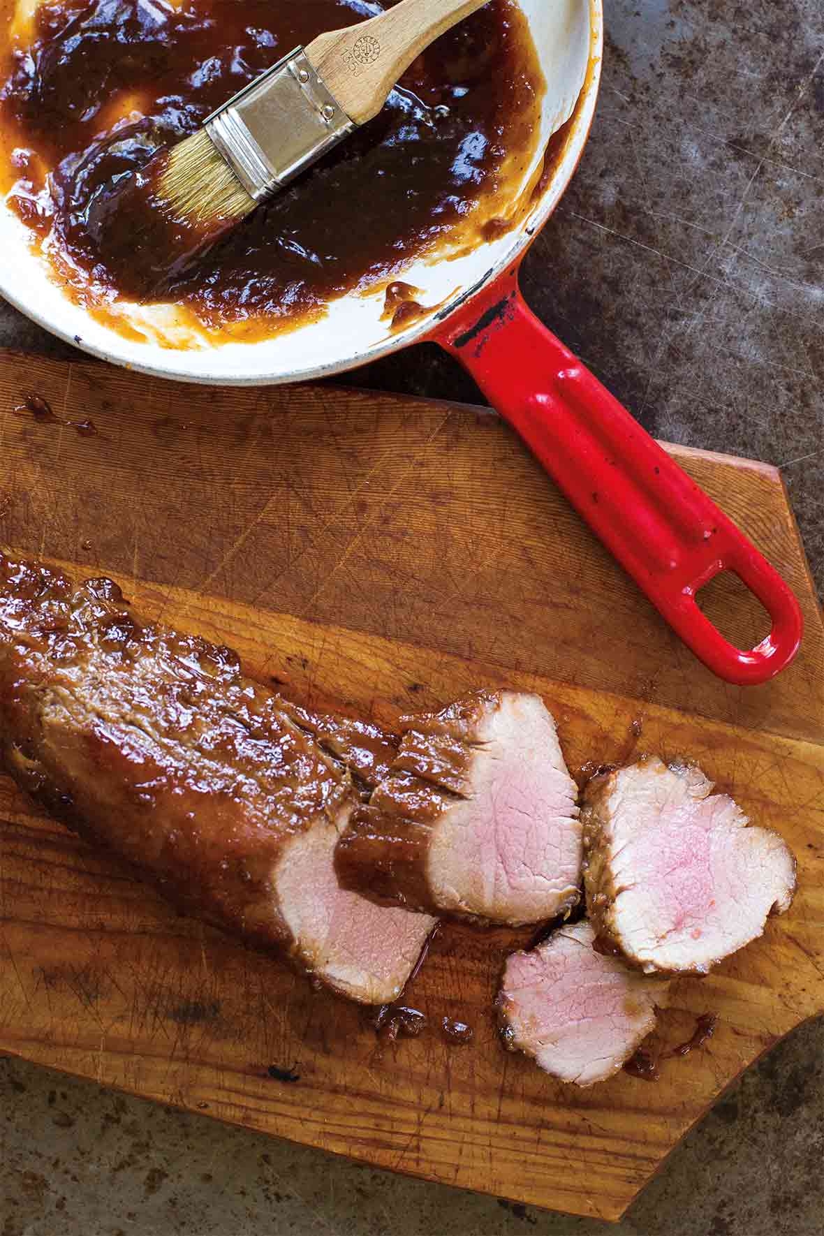 Cutting board with char siu pork--a pork tenderloin slathered with char siu sauce--and more sauce and the side