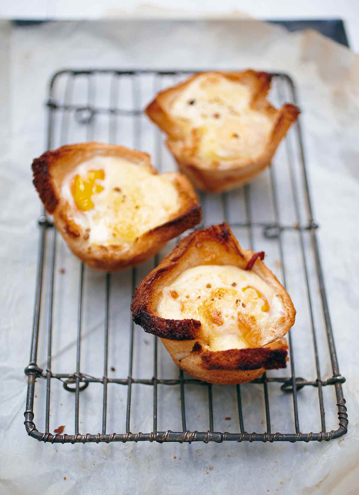 Three croque madame muffins on a wire rack, set over parchment paper.