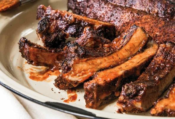 Plate of oven-baked barbecue ribs slathered in sauce with more sauce on the side