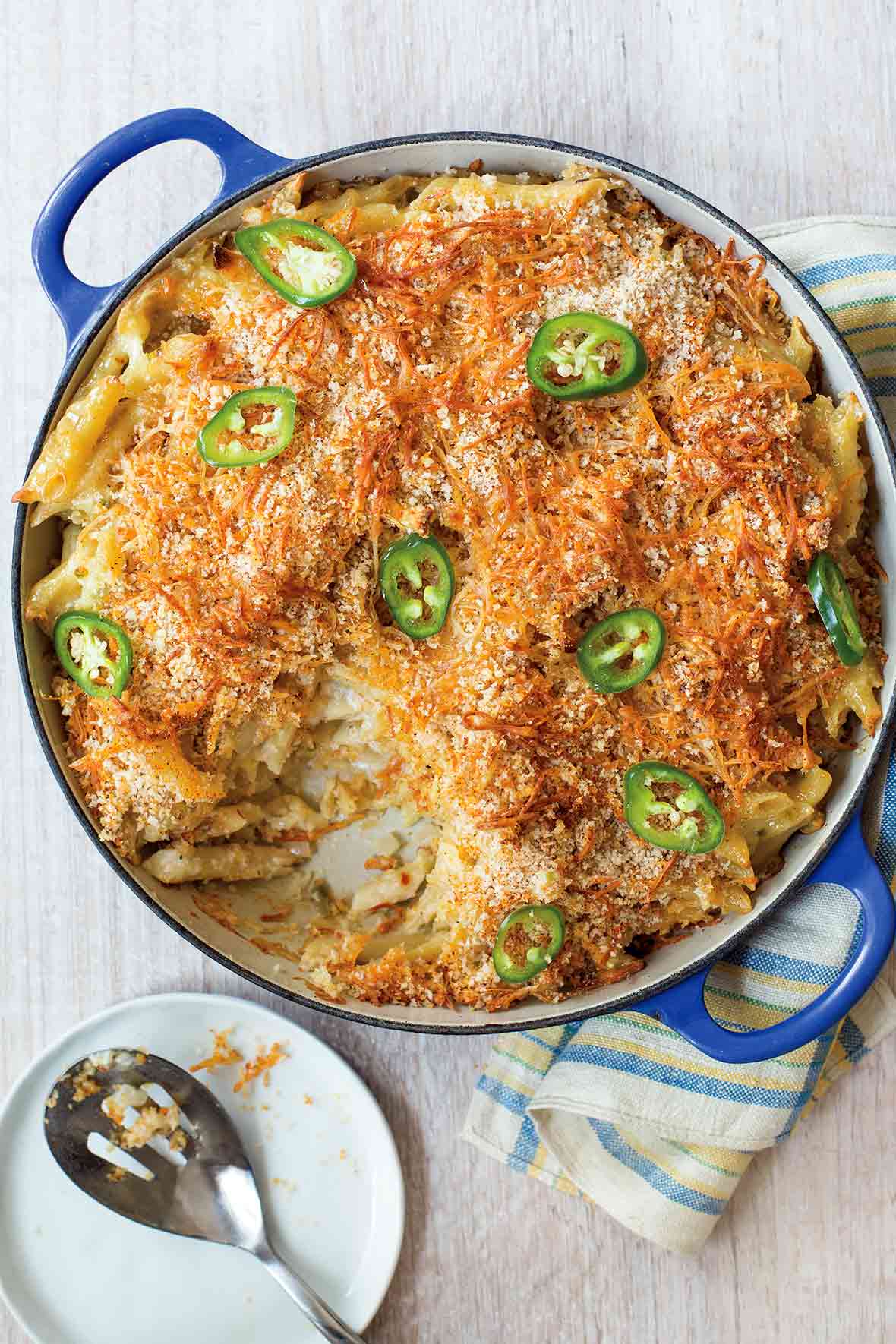 Blue casserole of spicy macaroni and cheese with breadcrumbs on top and sliced of jalapeno peppers
