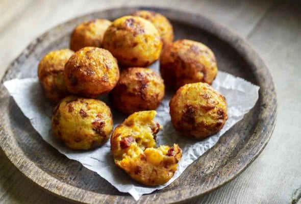 A wooden bowl filled with golf-ball-size fried potato and chouriço balls on a wooden tray