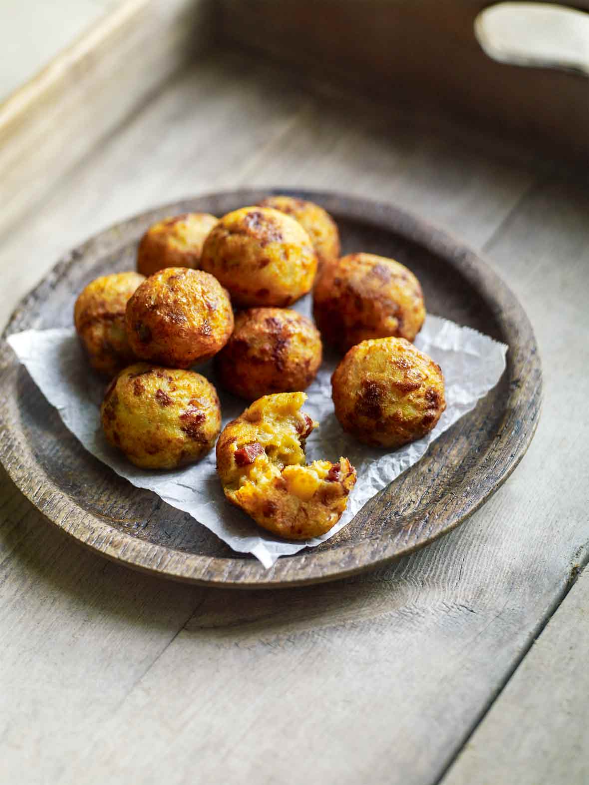 A wooden bowl filled with golf-ball-size fried potato and chouriço balls on a wooden tray