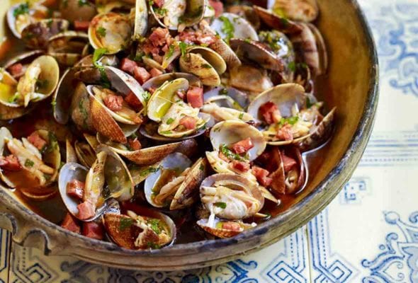 A bowl of clams with chouriço, garlic, and cilantro with a savory broth on top of blue and white tiles