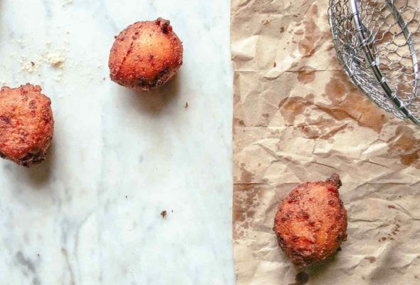 Three freshly fried hush puppies on a marble top and brown paper bag, a spider strainer bear by