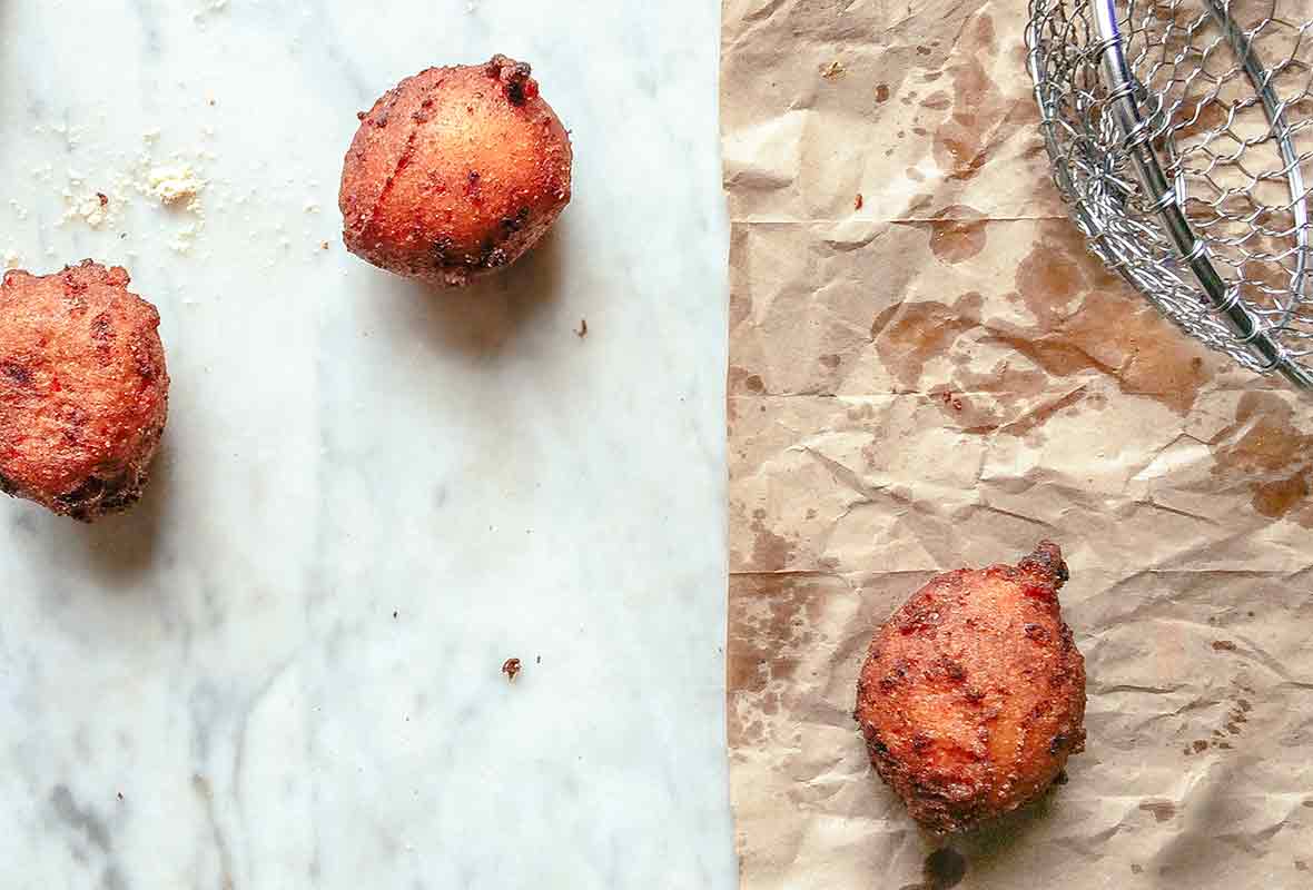 Three freshly fried hush puppies on a marble top and brown paper bag, a spider strainer bear by