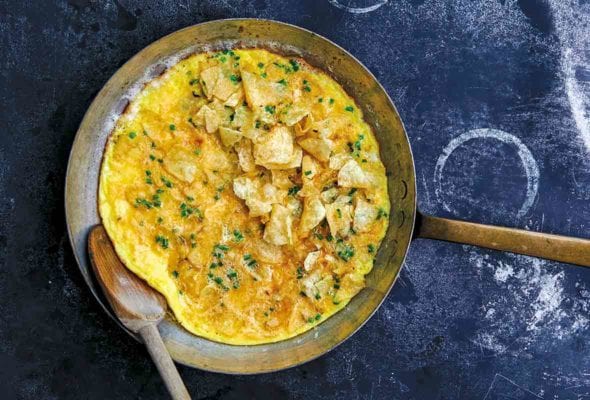 Copper skillet with a potato chip and chive omelet, a wooden spoon resting inside