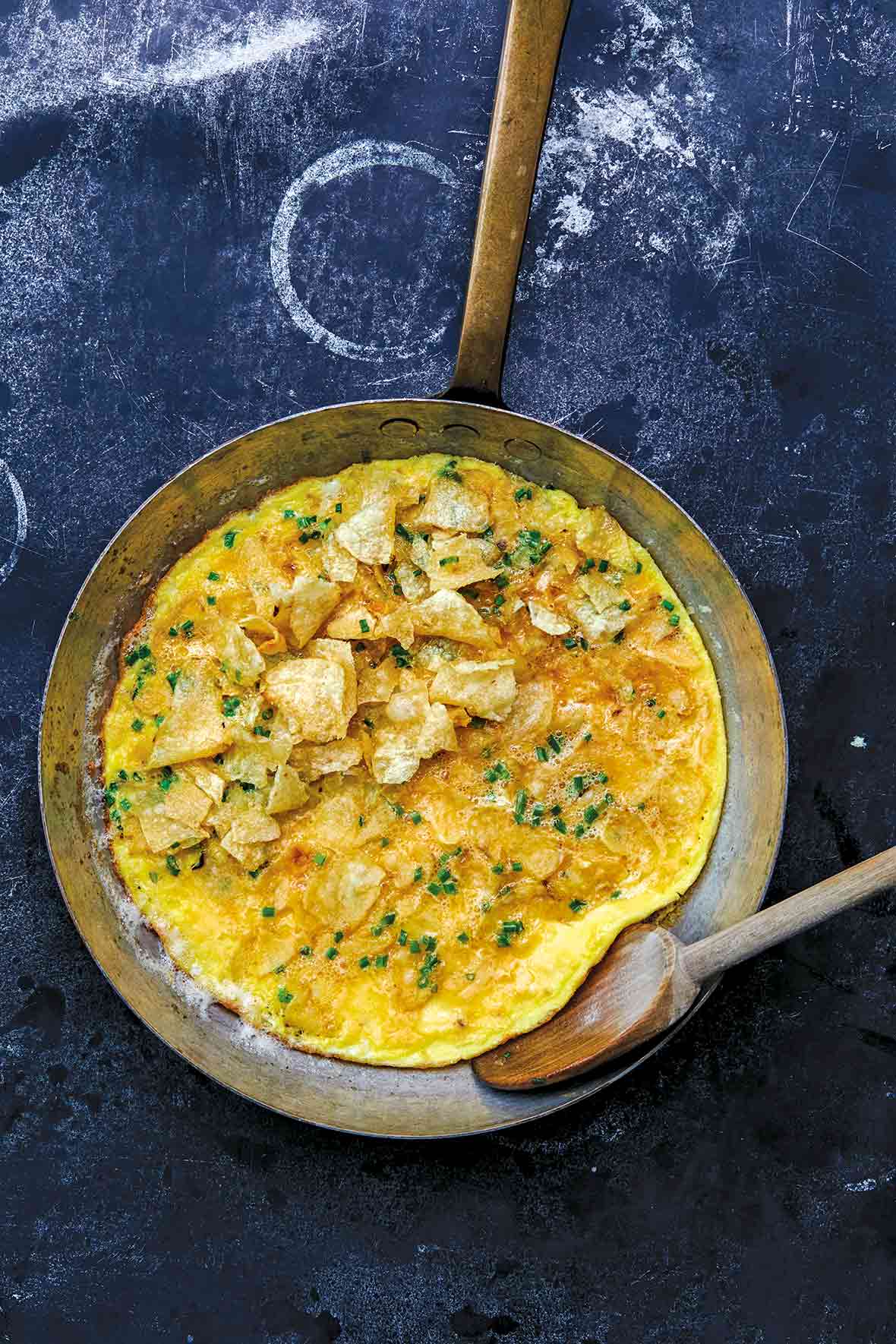 Copper skillet with a potato chip and chive omelet, a wooden spoon resting inside
