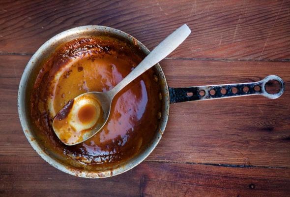 An empty pot and spoon with just a little spicy bourbon barbecue sauce at the bottom on wood