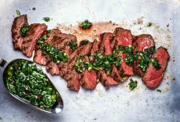 A sliced steak chimichurri with a gravy boat filled with chimichurri on the side.