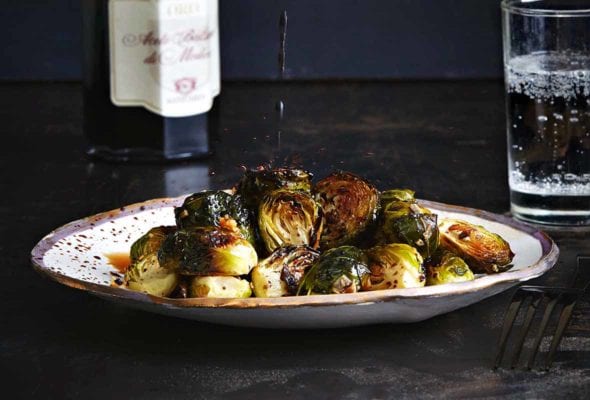 A plate of roasted Brussels sprouts with a drizzle of balsamic vinegar splashing down on it