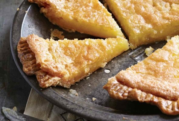 A chess pie with a homemade crust cut into four slices in an antique tin pie plate on top of a napkin