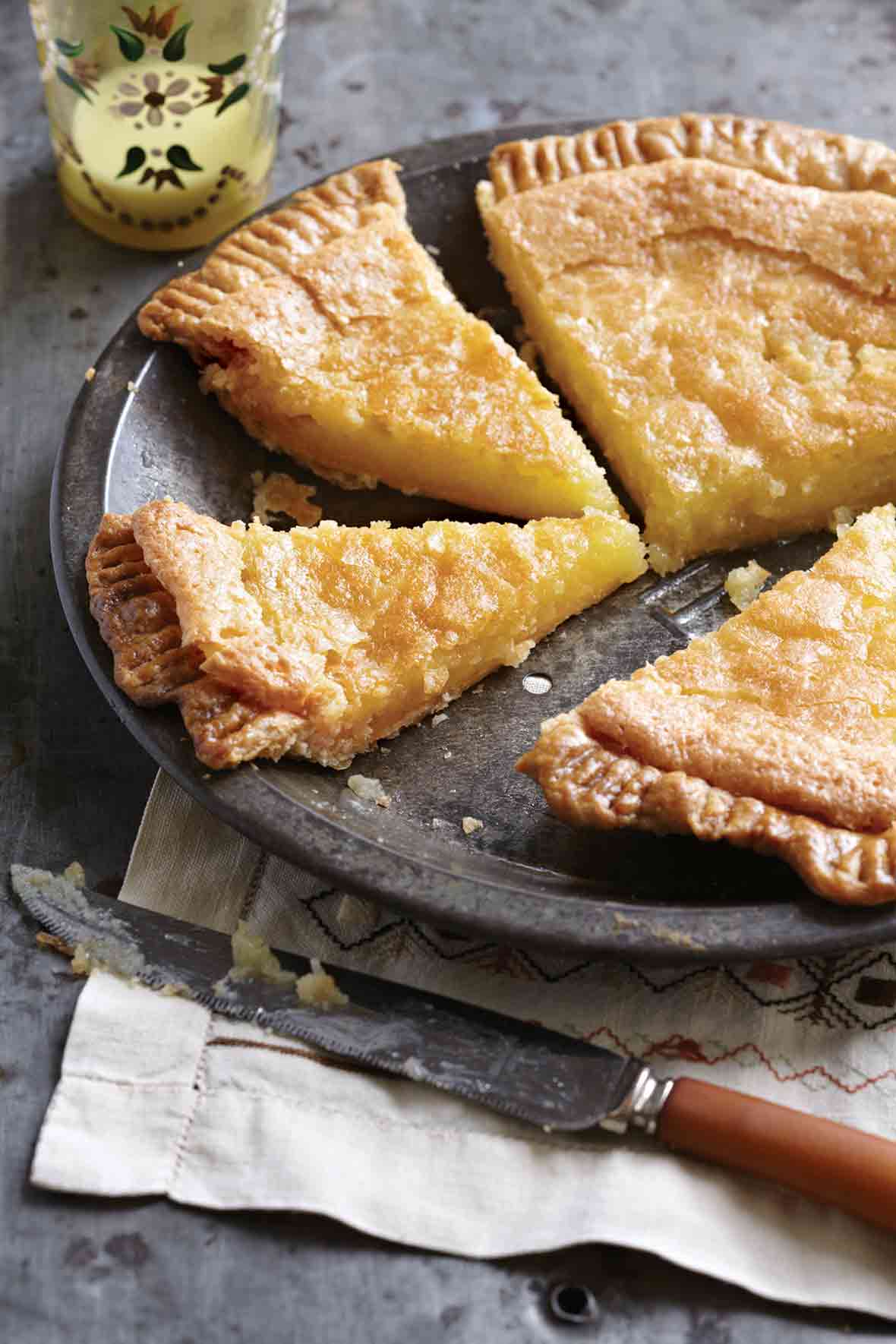 A chess pie with a homemade crust cut into four slices in an antique tin pie plate on top of a napkin