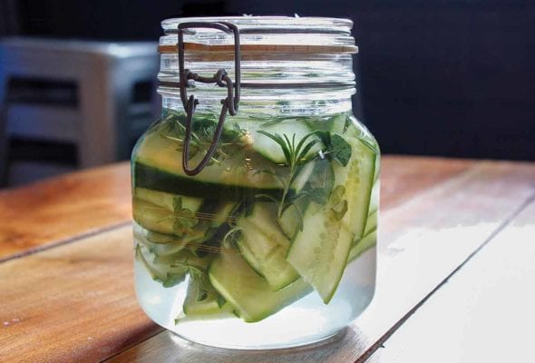 A small glass jar filled with sandwich pickles, rosemary, and thyme.