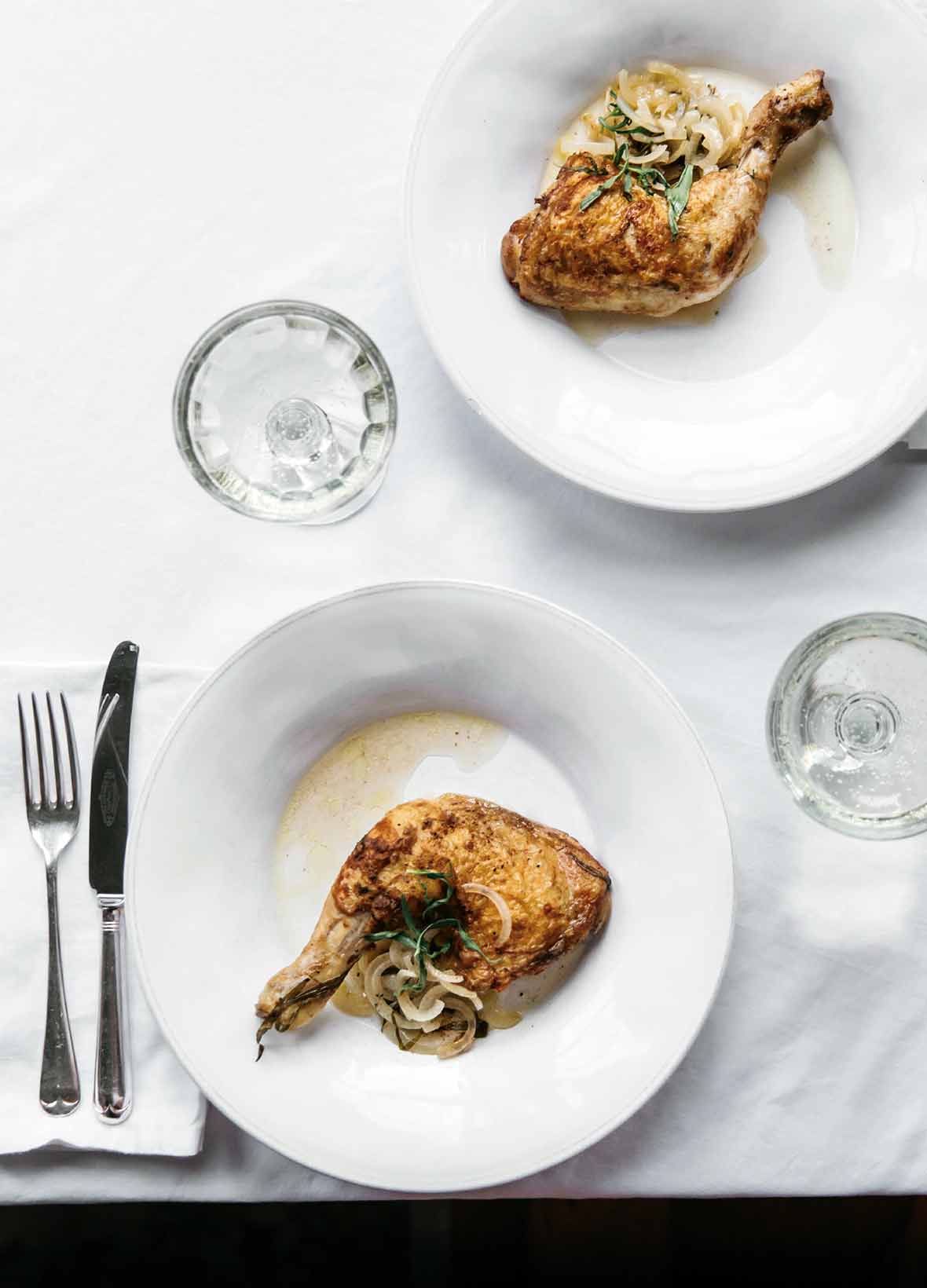 Two white plates with tarragon chicken leg and thigh on each, sliced onion and tarragon on top