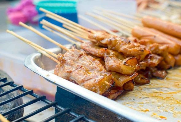 Skewers of thinly sliced Thai grilled pork or Moo Yang, on a metal tray in a street food vendor's cart