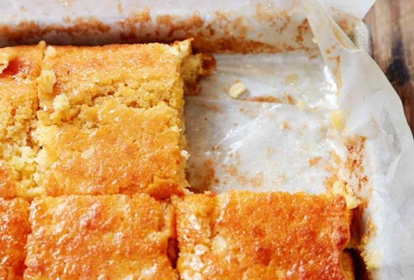 A parchment-lined square pan of buttermilk cornbread cut into squares, with one square missing.