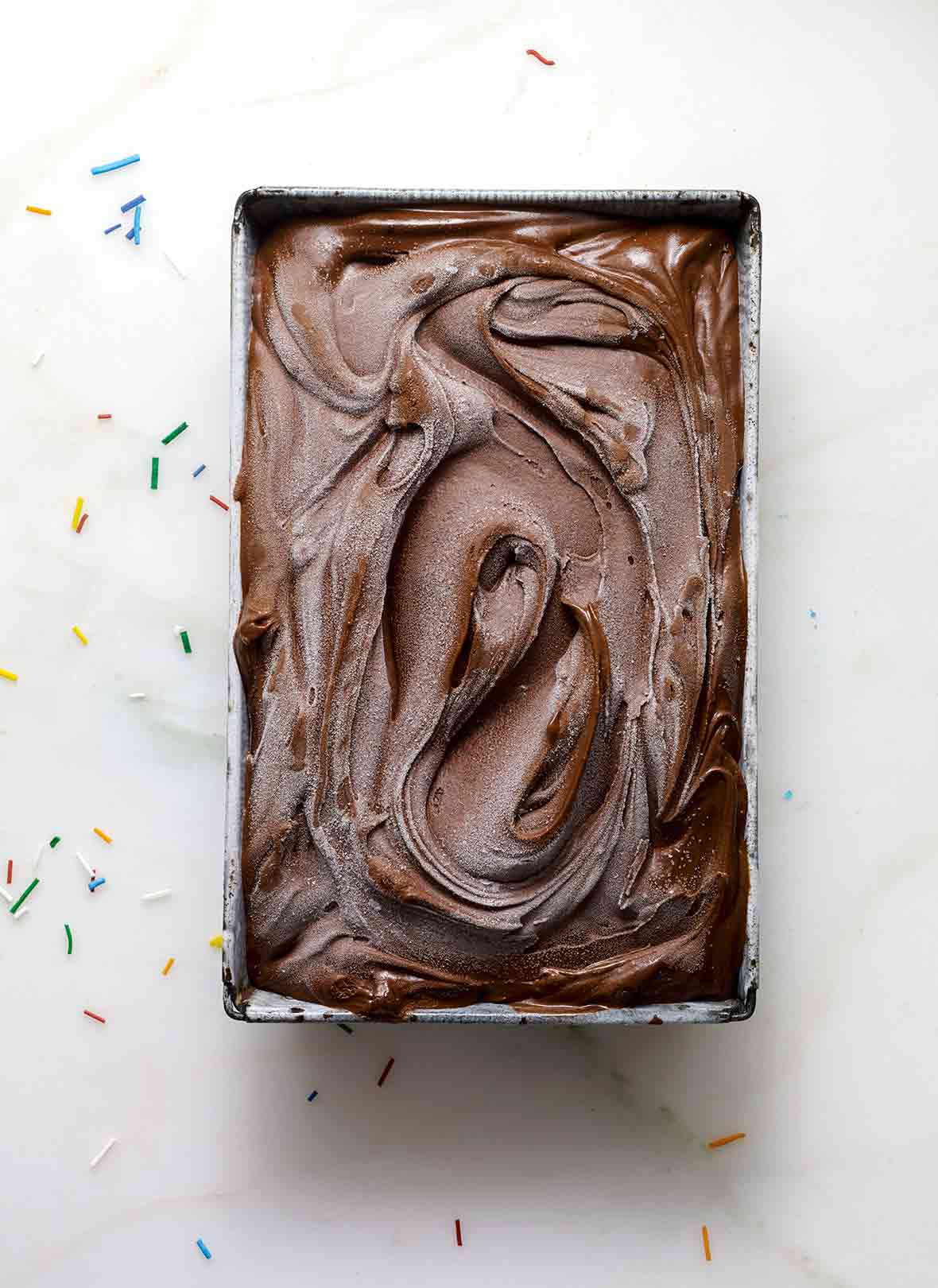 Metal loaf pan filled with swirls of dark devil’s food cake chocolate ice cream on a marble slab