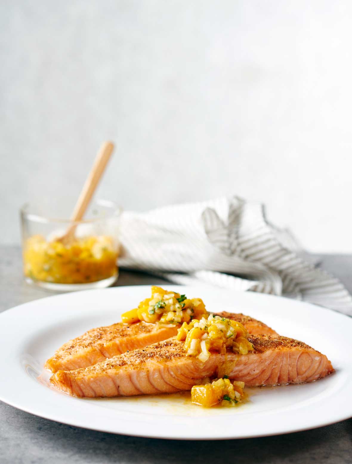 White plate with a fillet of Indian-spiced salmon with mango salsa on top