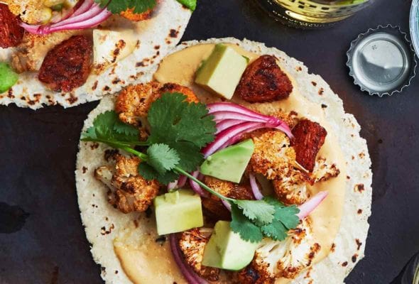 Two soft corn tacos filled with vegan cauliflower tacos al pastor--with pineapple chunks, pickled onions, cashew queso, avocado, cilantro