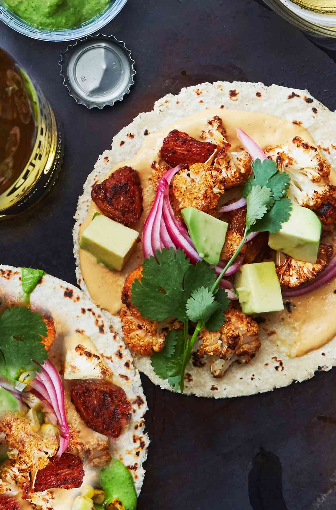 Two soft corn tacos filled with vegan cauliflower tacos al pastor--with pineapple chunks, pickled onions, cashew queso, avocado, cilantro