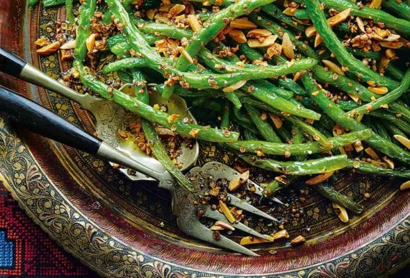An Indian-style platter with pan-fried green beans and almonds topped with ground coriander, nearby a serving fork and spoon