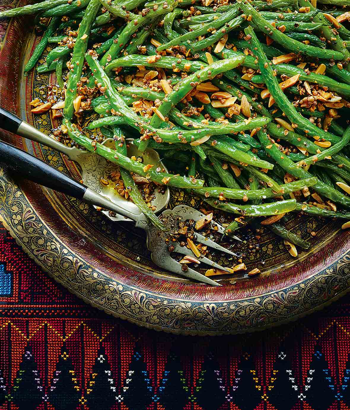 An Indian-style platter with pan-fried green beans and almonds topped with ground coriander, nearby a serving fork and spoon