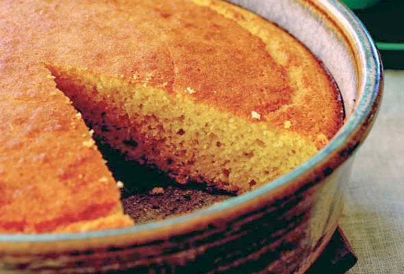 A cake pan of golden brown cornbread with a slice removed