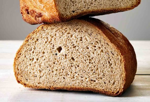 A loaf of Jewish rye bread, cur in half, one half balancing on the other