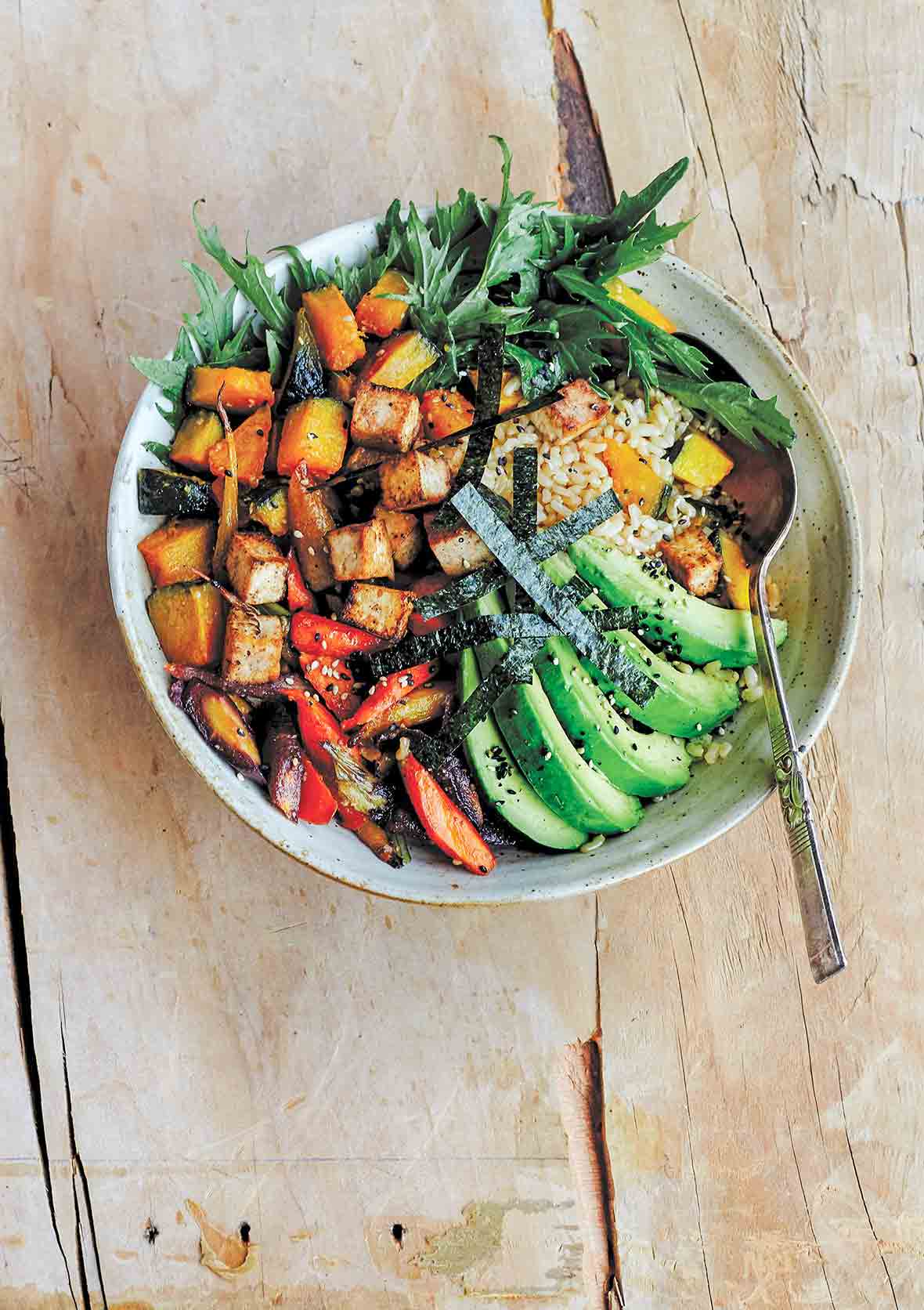 A bowl of miso-glazed kabocha squash with carrots, avocado, salad greens, seaweed over brown rice