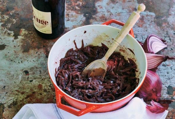 A red Le Creuset pot filled with red wine onions, that have been slowly cooked together