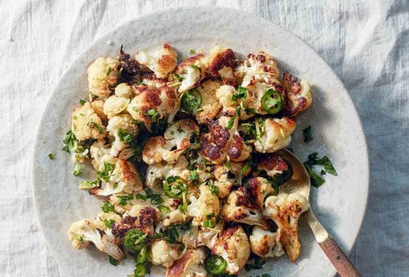 A white plate of roasted cauliflower, sliced jalapeno peppers, parsley, with a fork