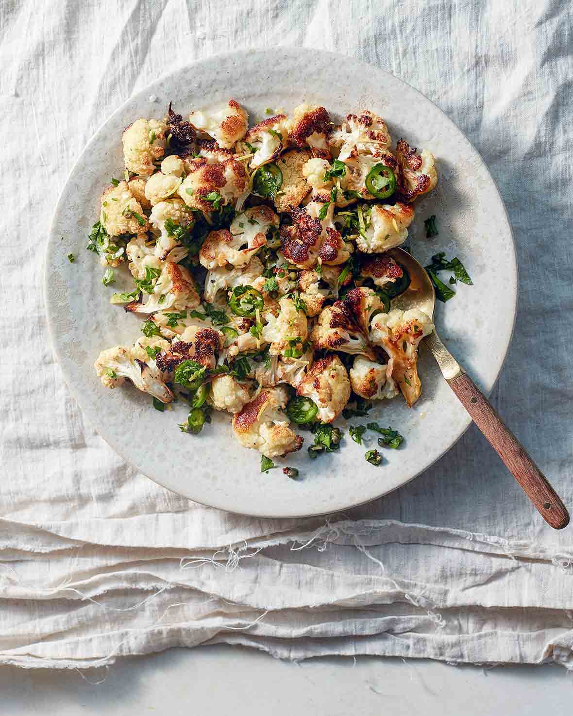 A white plate of roasted cauliflower, sliced jalapeno peppers, parsley, with a fork