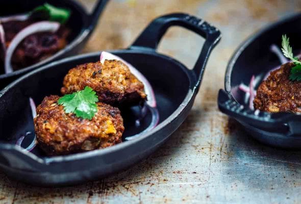 Three small blue plates filled with spicy beef kebabs, red onion, and cilantro
