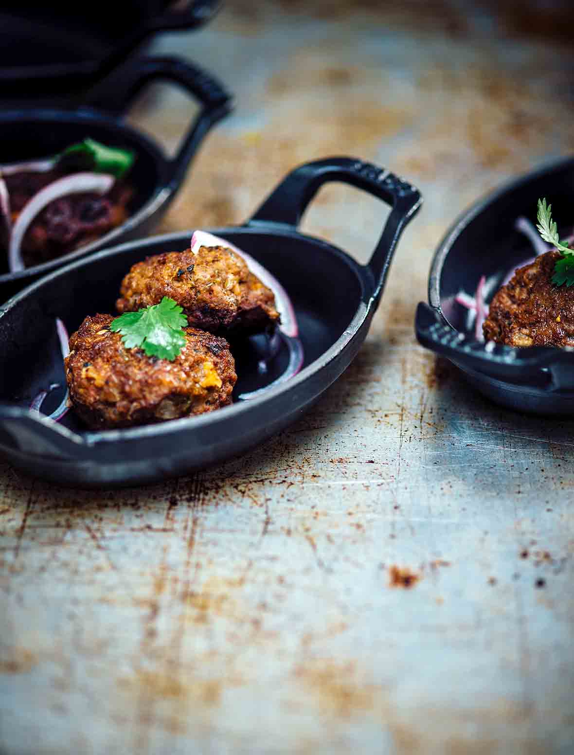 Three small blue plates filled with spicy beef kebabs, red onion, and cilantro