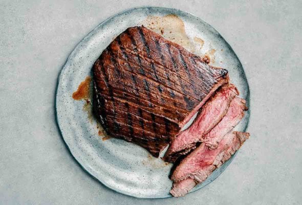 An Asian grilled flank steak, with several medium rare sliced cut from it, the outside crisscrossed with grill marks--on a plate