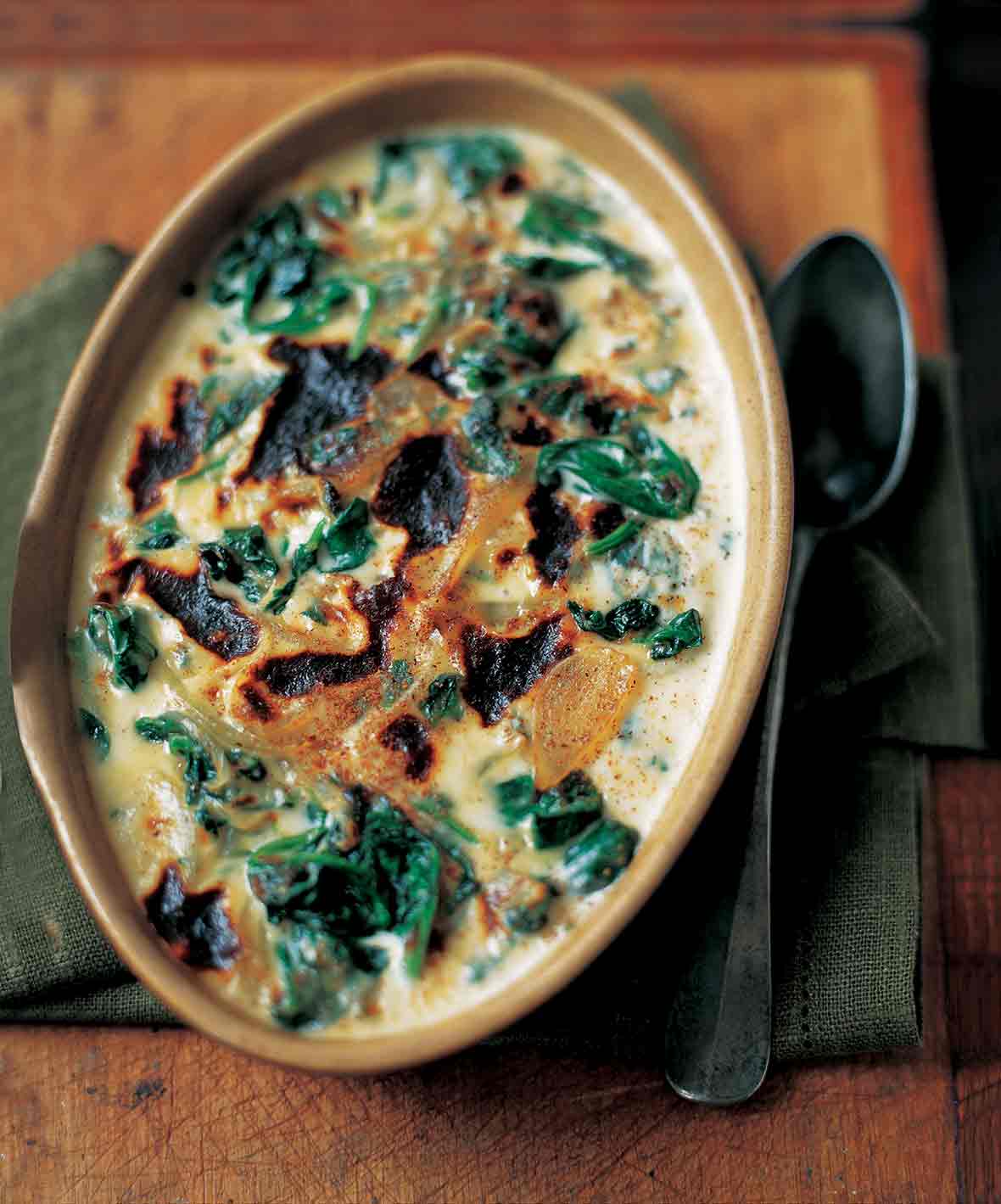 A ceramic oval dish of baked spinach mornay with cream sauce, sliced onion, and browned top