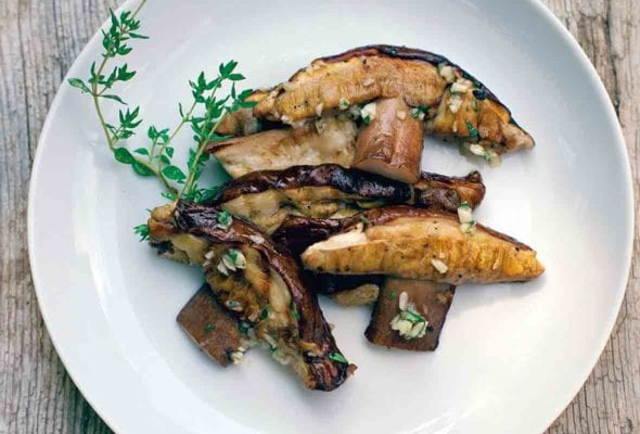 A white plate filled with sliced grilled porcini mushrooms with mint and garlic, garnished with a sprig of thyme.