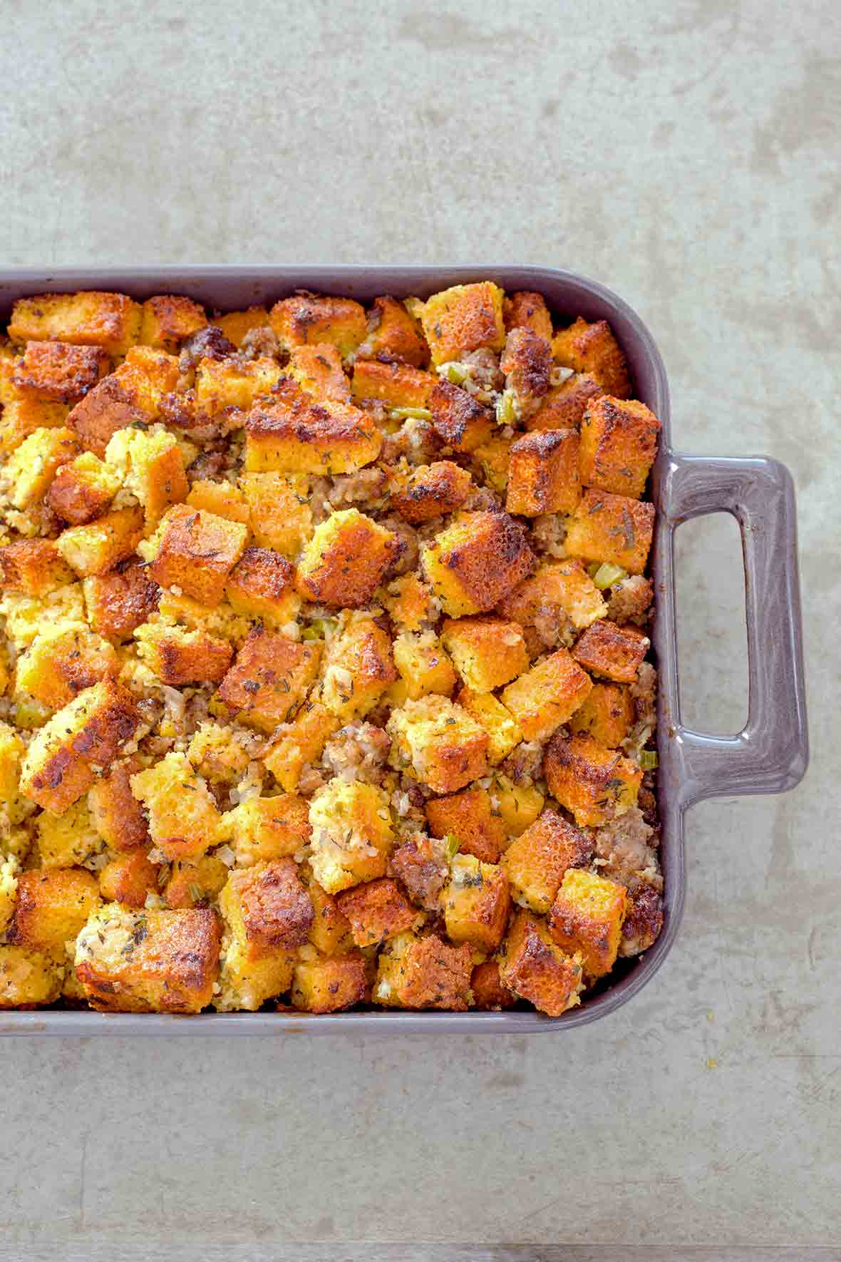 Casserole dish of cubes of homemade cornbread sausage dressing, with pork sausage, onion, celery, and spices