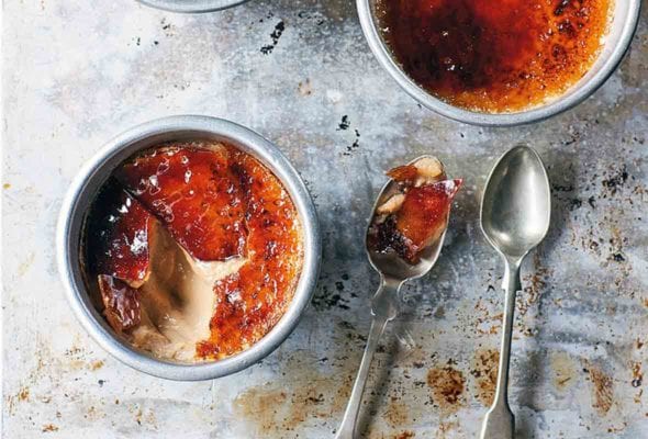 Two ramekins filled with masala chai creme brûlée, one with it's top cracked open to reveal the creamy inside