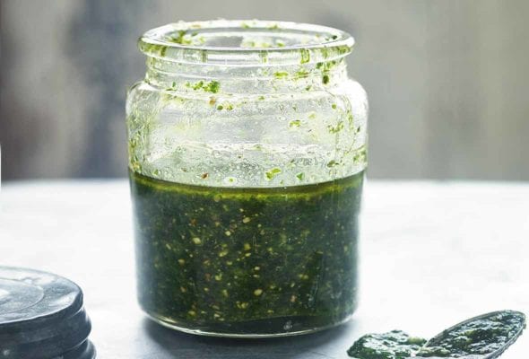 Glass jar of pumpkin seed pesto, nearby the lid and a spoon with pesto