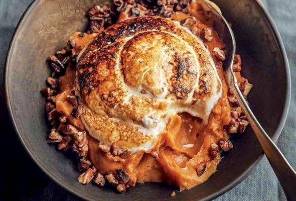 A bowl of sweet potato puree with marshmallow, which is toasted with a torch, toasted buttered pecans around the edge