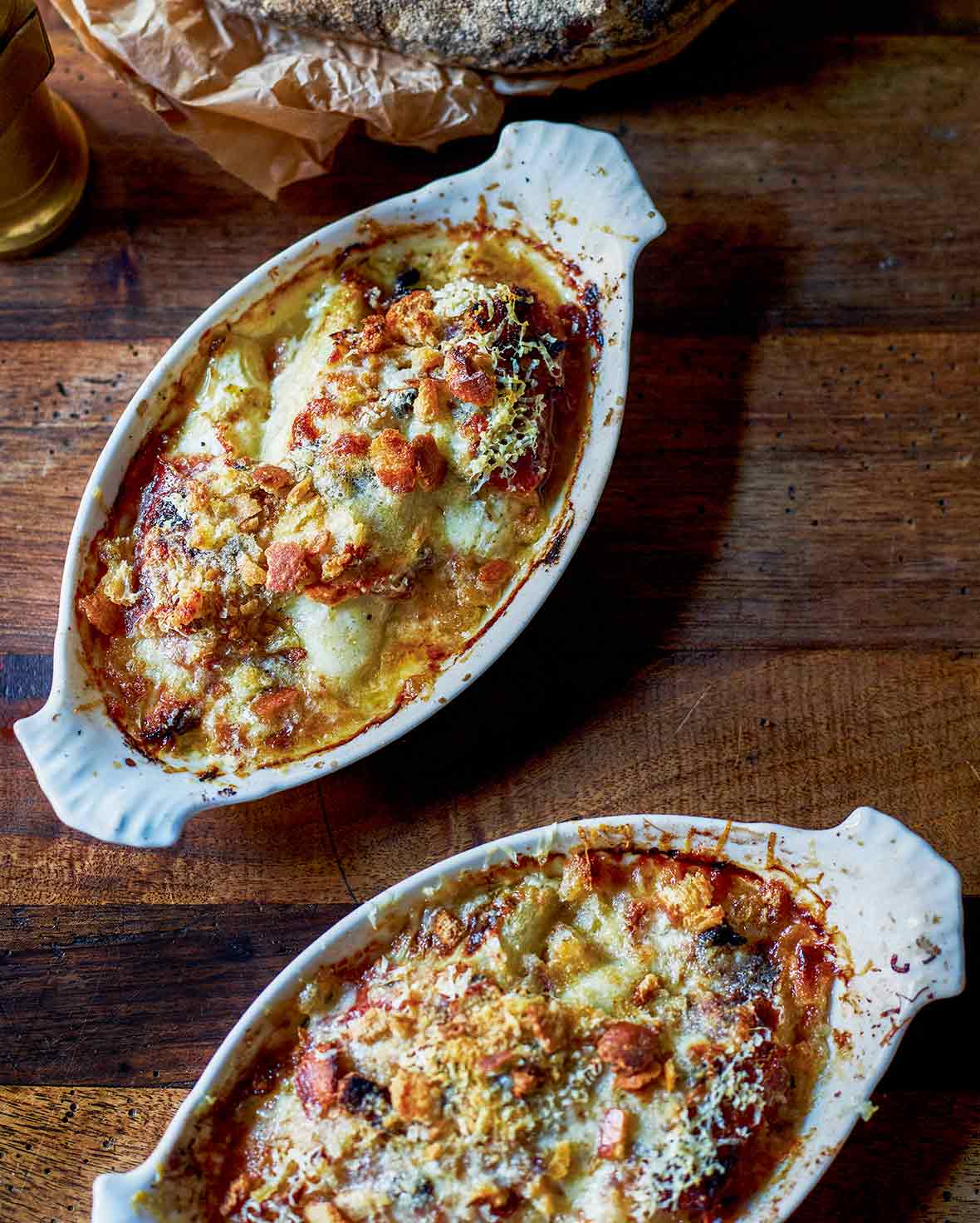 Two oval gratin dishes filled with braised endive gratin topped with bubbly browned cheese and breadcrumbs