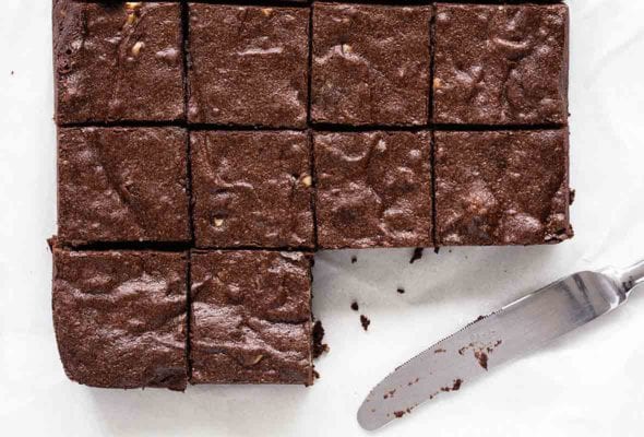 10 fat, chocolatey fudgy pudgy brownies sliced, with a table knife nearby with crumbs