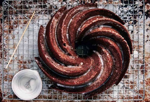 A swirled gingerbread Bundt cake with a lemon glaze on top, all on wire rack over a sheet pan