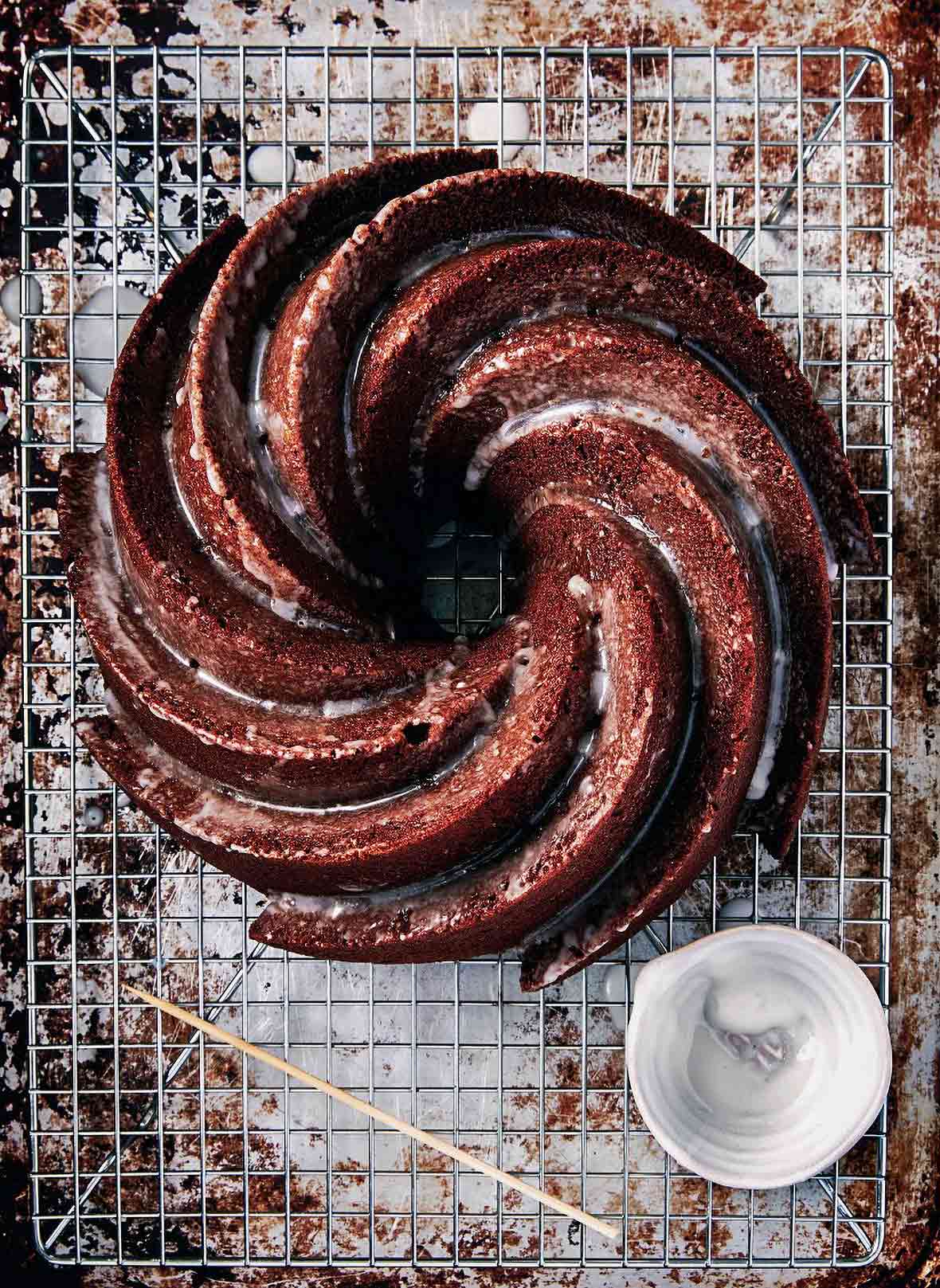 A swirled gingerbread Bundt cake with a lemon glaze on top, all on wire rack over a sheet pan